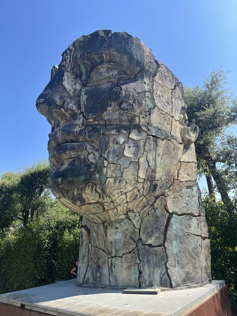 Igor Mitoraj's Tindaro Screpolato (1997) shot head-on from the visitor path, the cracked bronze face of Tyndareus rising above its Corten plinth in the Boboli Gardens, Florence