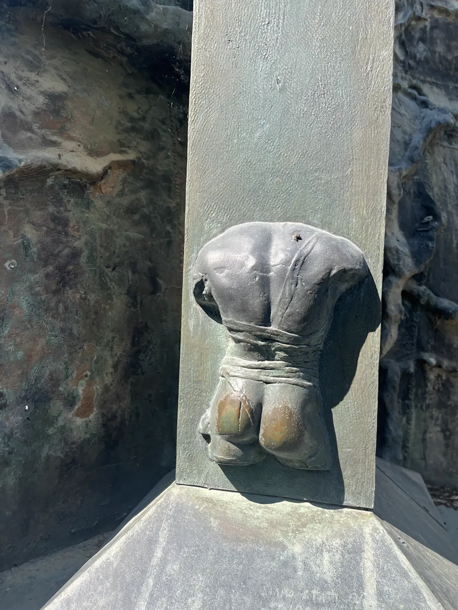 Detail of a smaller Mitoraj bronze figure — a headless torso with a wrapped waistband — set within a scored bronze frame, Florence, July 2026