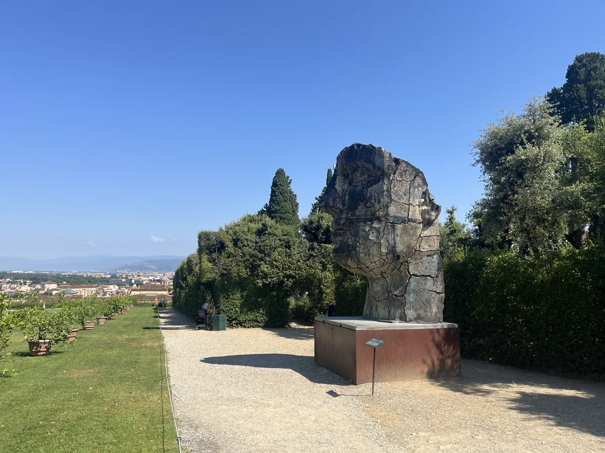Wide landscape framing of the upper Boboli terrace with Tindaro Screpolato just visible at right, the gravel walkway and cypress line stretching away into the garden
