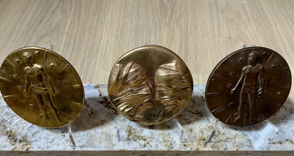 La Conversation — Igor Mitoraj, three specimens on granite: gilt reverse (left), worn obverse (centre), dark brown reverse (right)