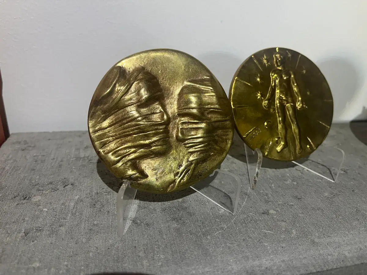 La Conversation — Igor Mitoraj, both medal variants on acrylic stands, obverse and reverse side by side