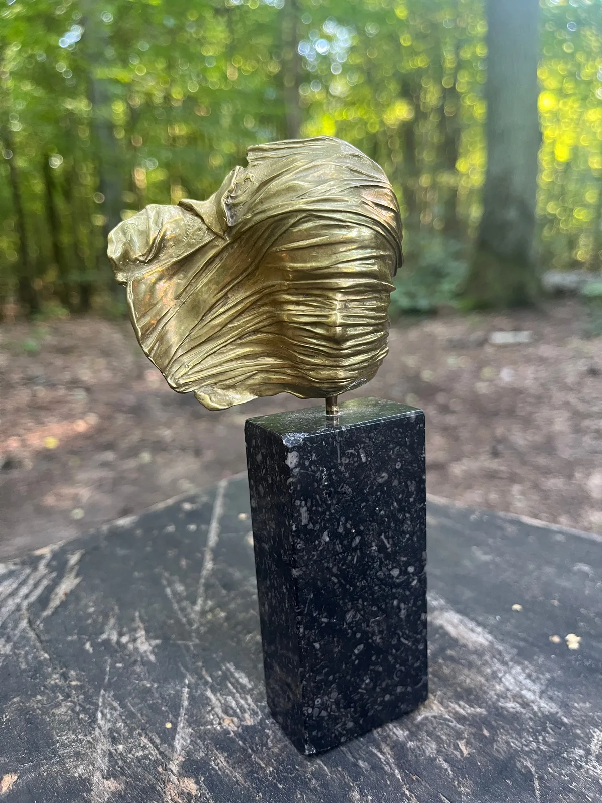 Visage Voilé — Igor Mitoraj, gilded bronze on dark marble base, forest bokeh backdrop